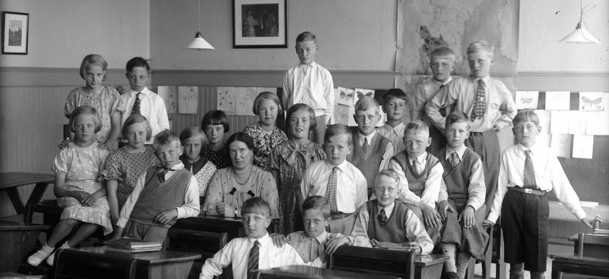 En skolklass med sin lärarinna i mitten. Pojkarna i skjorta och slips. Flickorna i klänningar.